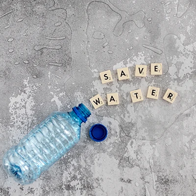 Scrabble letters spelling 'Save Water' next to a plastic bottle with spilled water